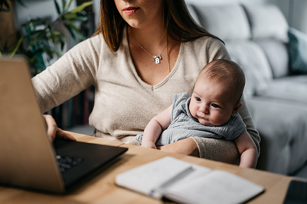 Tiffany working at a laptop while holding her baby